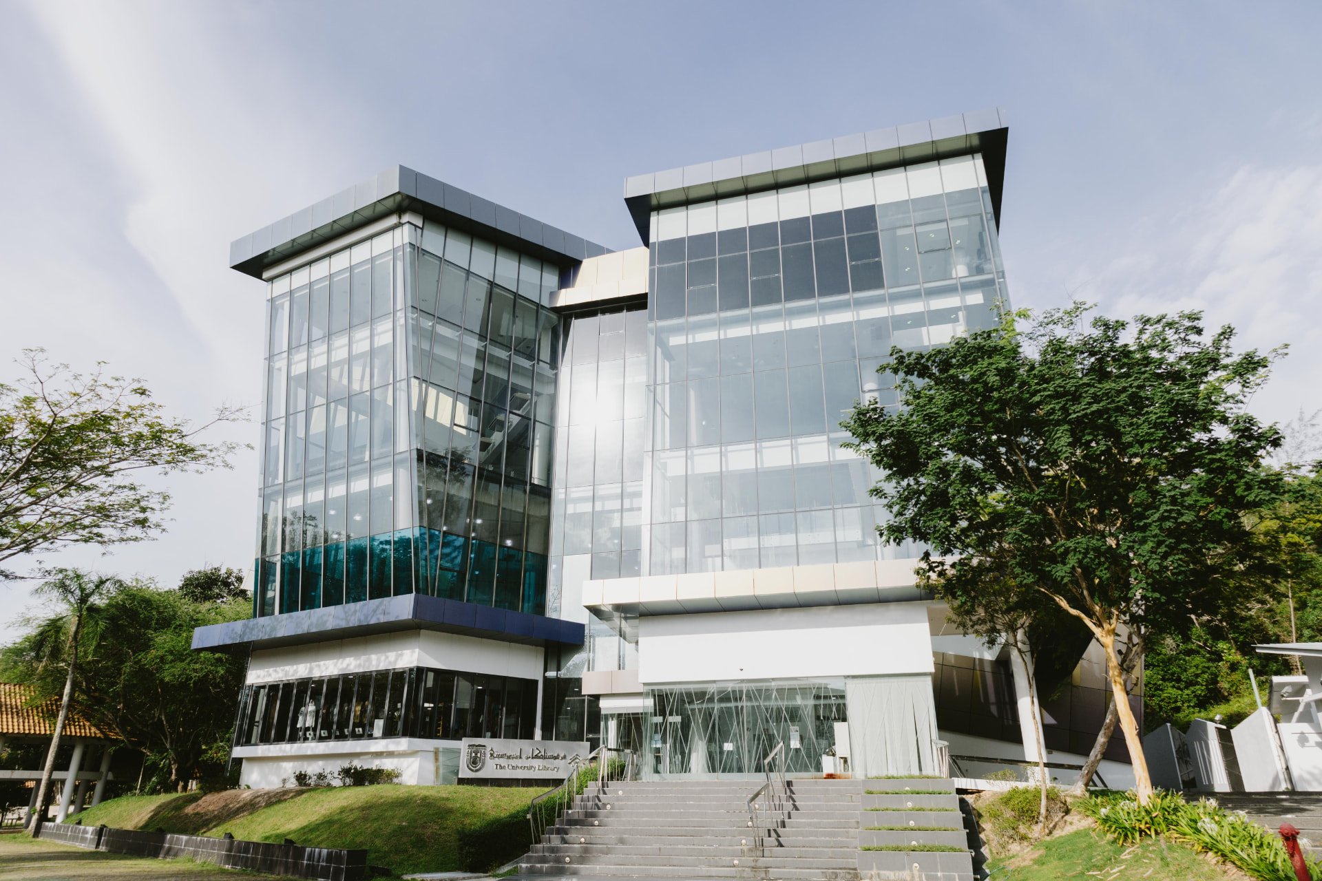 The glass towers and main entrance of the University Library at Universiti Brunei Darussalam, framed by trees.